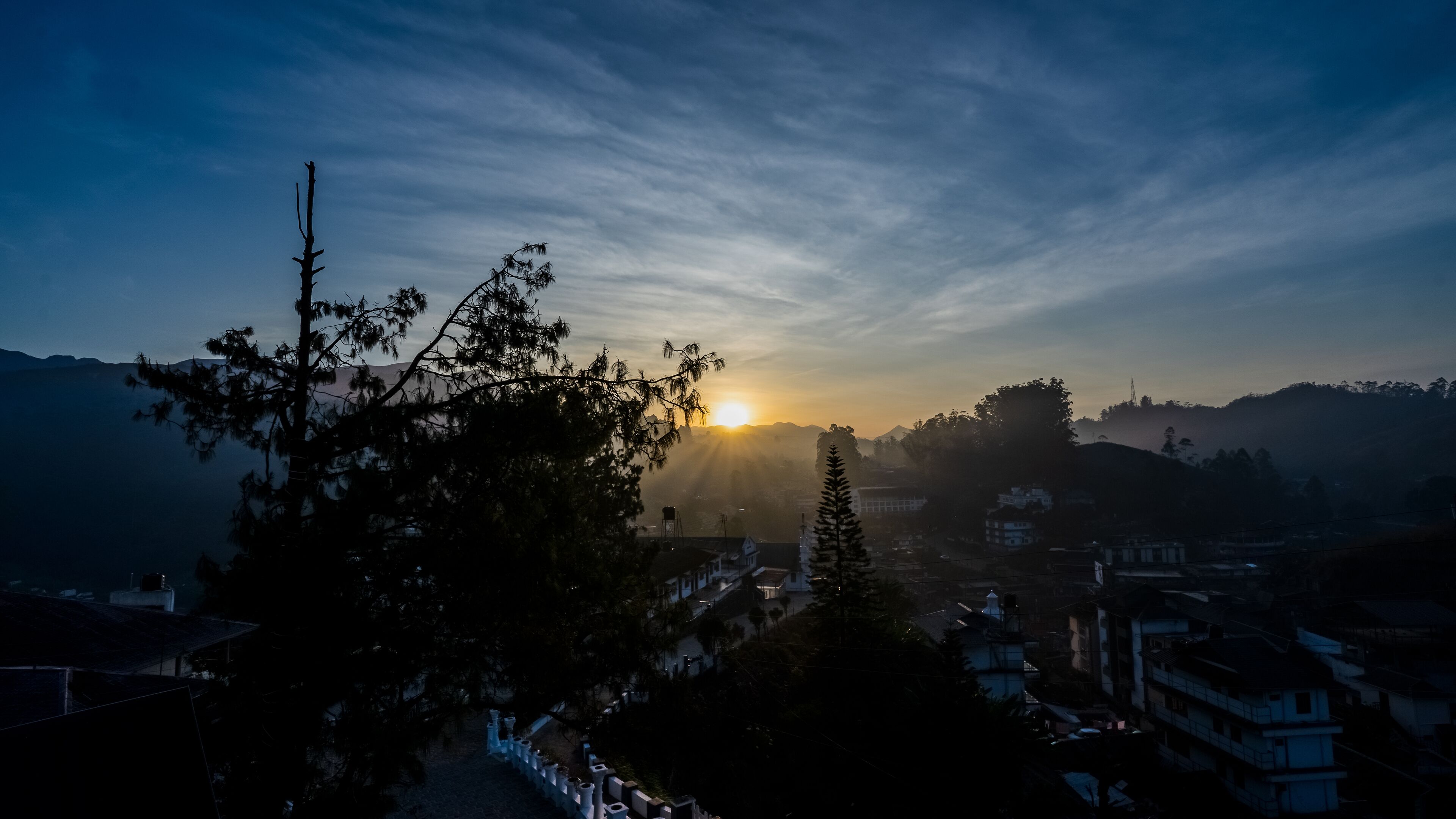 Aquest cel s'il·lumina amb un sol ixent sobre un paisatge montanyós, amb edificis al primer pla.