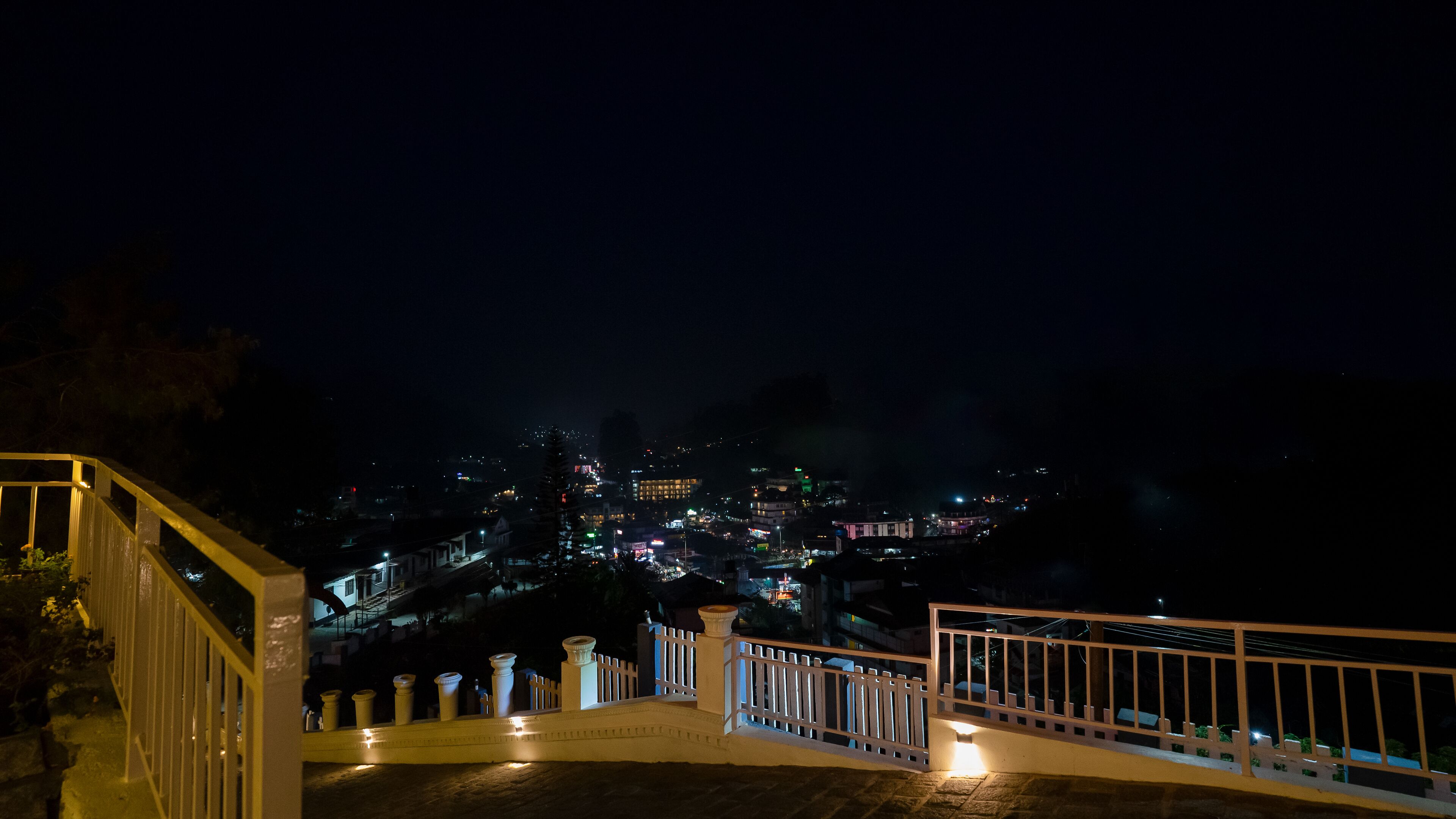 A nighttime view of a cityscape from a balcony with a railing.