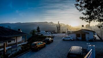 Un área de estacionamiento con varios coches, un edificio con el letrero "KAYAL PLUS CHILOLING" y una vista de montañas al fondo.