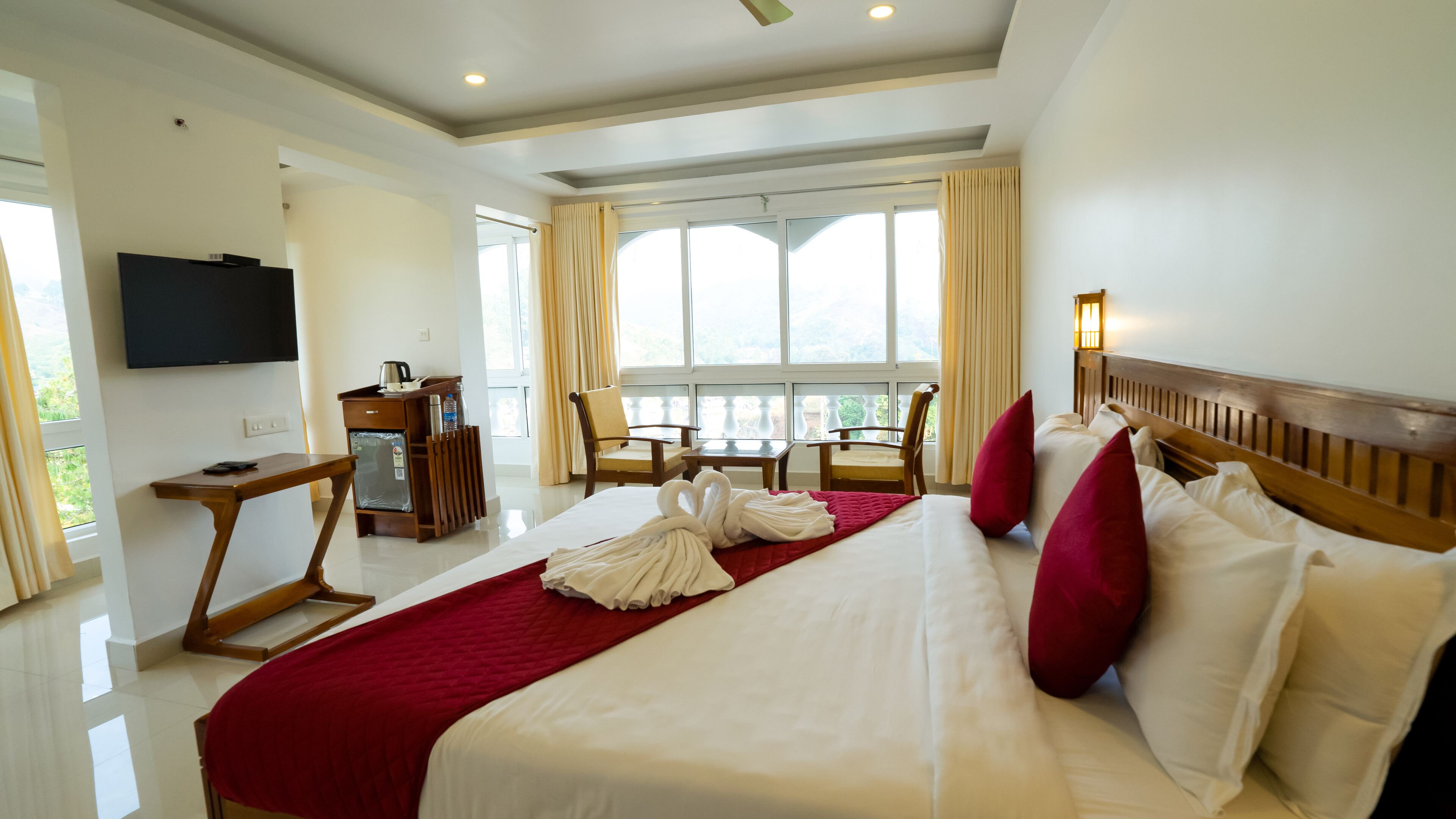 A hotel room with a large bed, a desk, a TV, and a balcony with chairs.