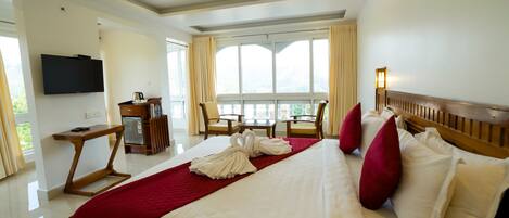 Quarto de hotel com uma cama grande, uma mesa, uma TV e uma varanda com cadeiras.