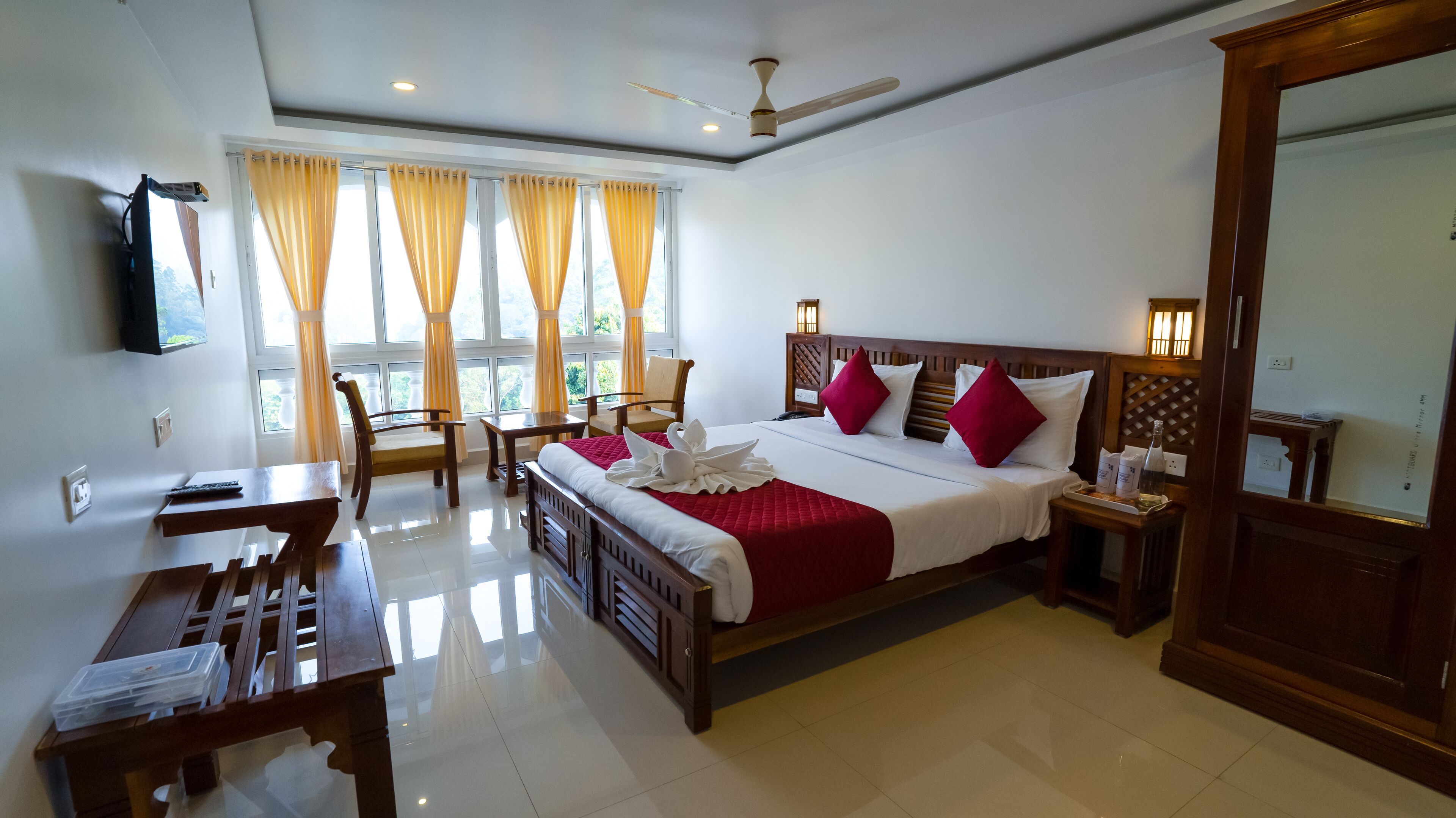 Habitación de hotel con cama, escritorio, silla, mesa, televisor y ventana con cortinas.
