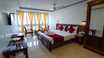 Habitación de hotel con cama, escritorio, silla, mesa, televisor y ventana con cortinas.