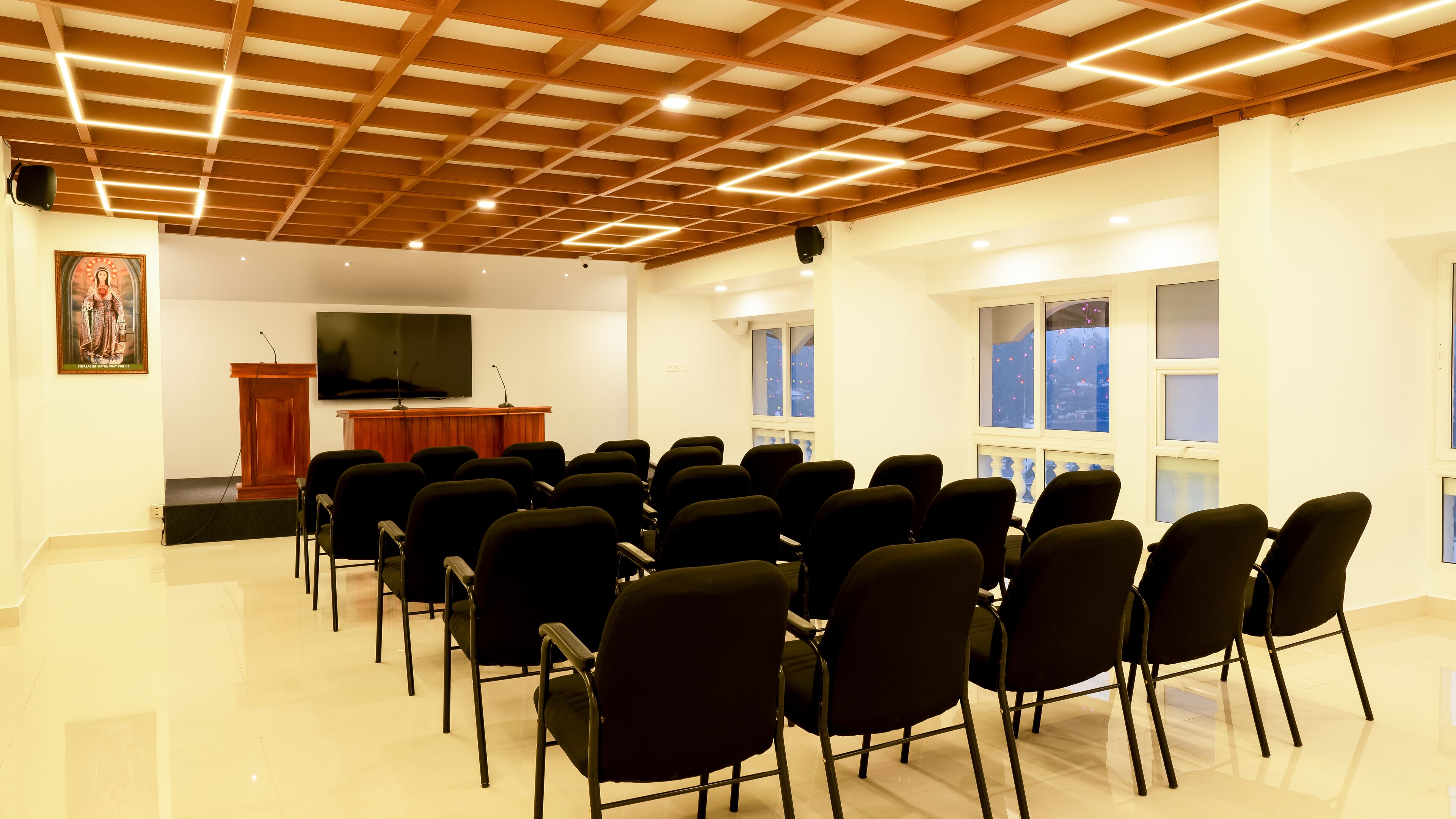 Une salle de conférence avec un plafond en bois, un pupitre, un grand écran et des rangées de chaises.