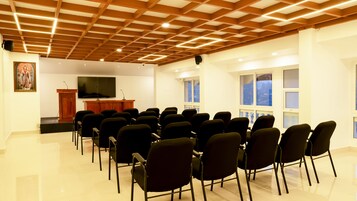Uma sala de conferências com teto de madeira, um palanque, uma tela grande e fileiras de cadeiras.