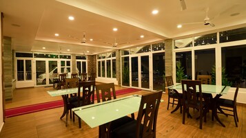 A spacious dining area with glass tables and wooden chairs, large windows, and a stone accent wall.