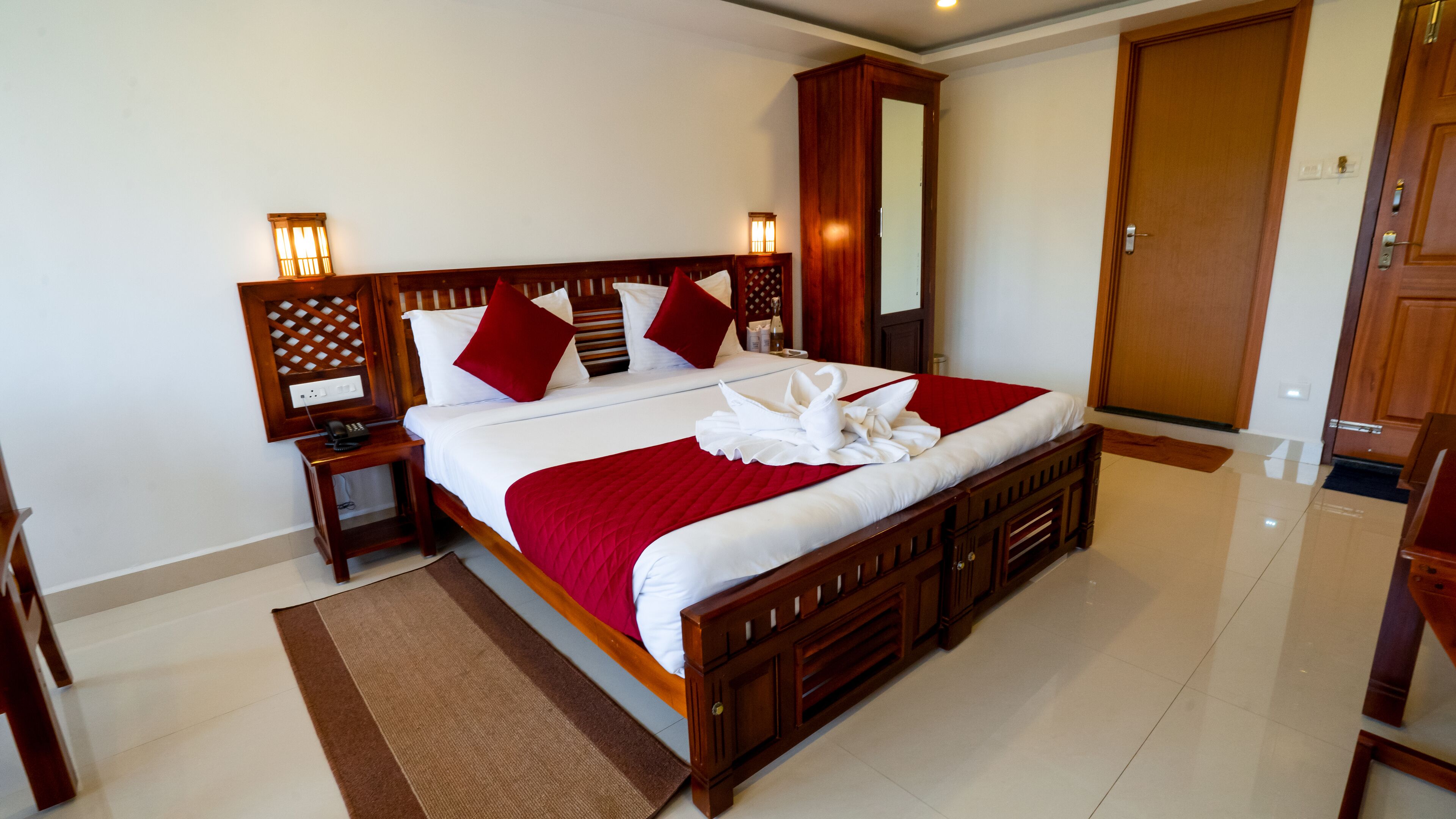 A spacious hotel room with a large bed, wooden headboard, bedside tables, and a wardrobe.