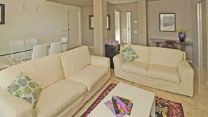 A modern living room with two cream-colored sofas, a glass dining table, and a coffee table with magazines. - Blu View Apartment in Salo (Salò)