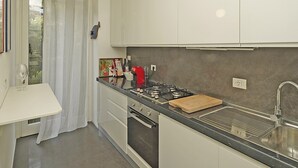 A modern kitchen with white cabinets, a black countertop, a red pendant light, and a window with a view of greenery. - Blu View Apartment in Salo (Salò)