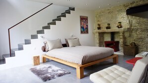 A modern bedroom with a wooden bed, a stone fireplace, and a staircase. - La Demeure de Saint Fiacre (Saint-Fiacre-sur-Maine)