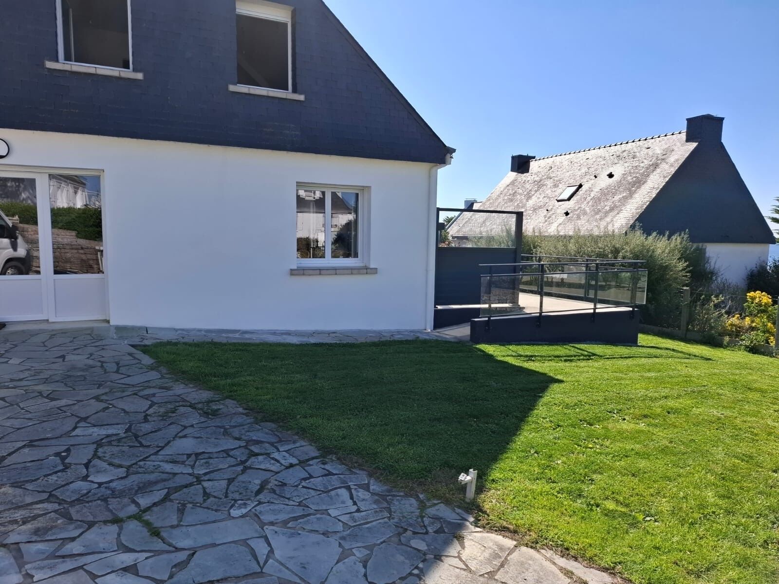 A modern house with a stone pathway leading to a white door, a well-maintained lawn, and a clear sky.