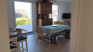 Amplia habitación con una mesa de comedor, sillas, un banco, televisión y vistas al exterior.