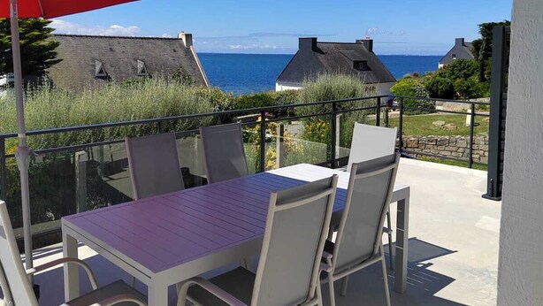 Un patio con una mesa, sillas, un paraguas rojo y vista al mar.