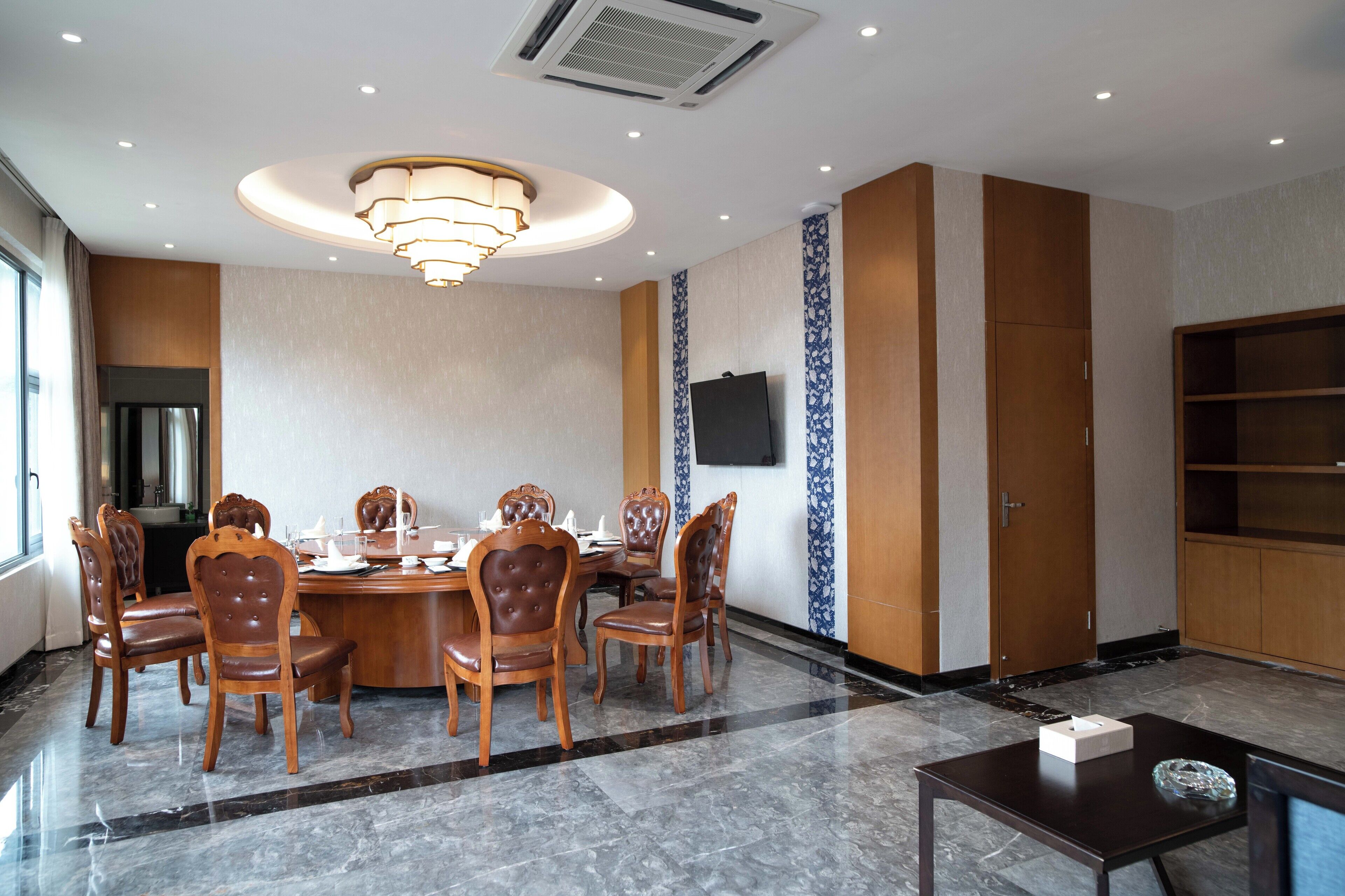 A conference room with a round table, wooden chairs, a television on the wall, and a large bookshelf.