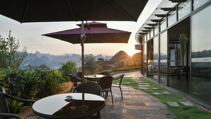 A patio with outdoor seating, a large umbrella, and a view of mountains. - Guizhou Fenglin Yueshan Hotel (Qianxinan Buyei and Miao)