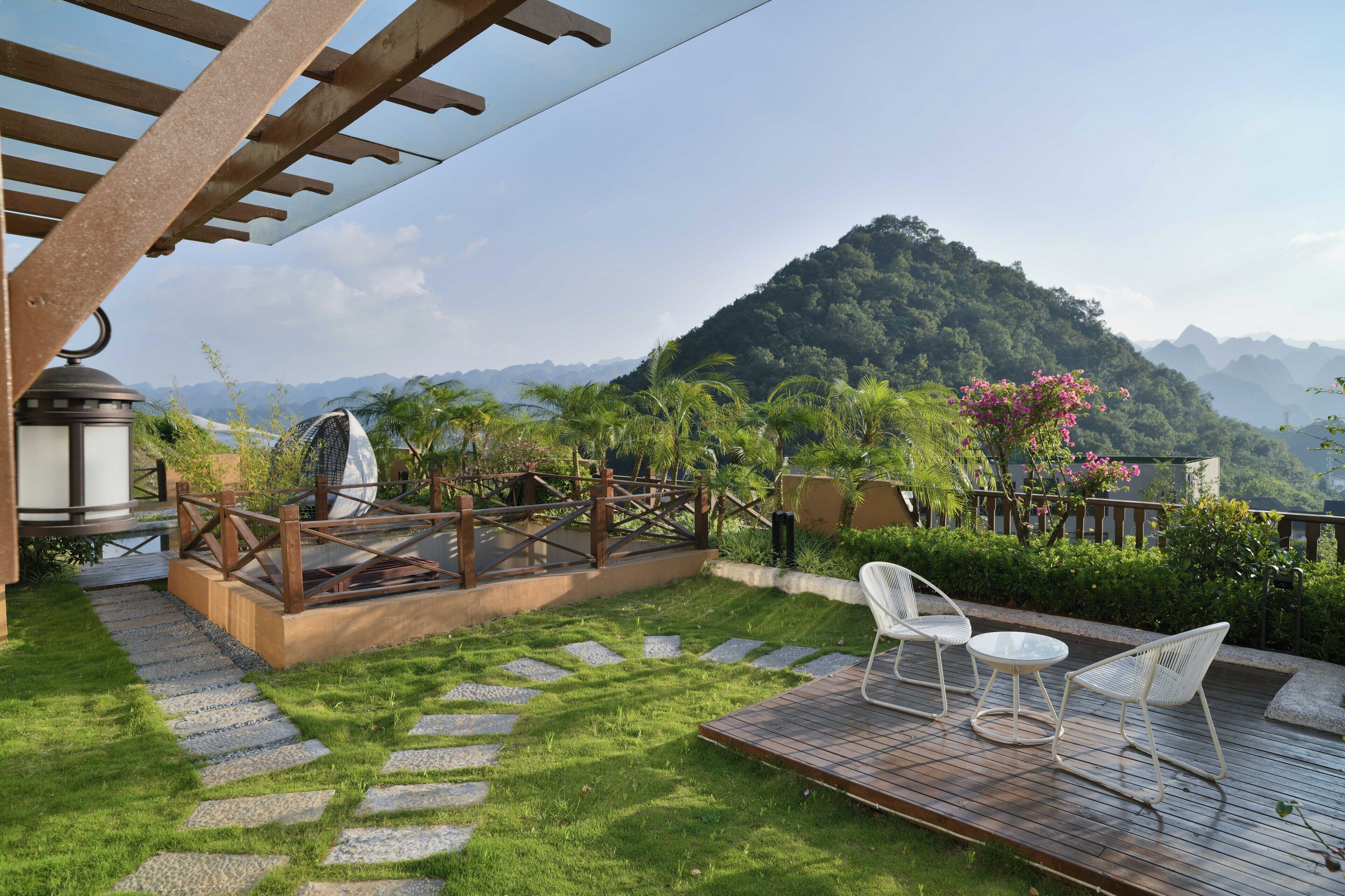 A patio with a pergola, a small table, two chairs, and a view of a mountain.