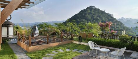 A patio with a pergola, a small table, two chairs, and a view of a mountain.