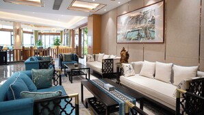 A spacious lobby with a sofa set, coffee table, and chairs. There is a large framed artwork on the wall and a decorative statue. - Guizhou Fenglin Yueshan Hotel (Qianxinan Buyei and Miao)