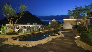 A nighttime view of a landscaped area with a reflective pool, a wooden bridge, and a building with a dome-like structure. - Guizhou Fenglin Yueshan Hotel (Qianxinan Buyei and Miao)