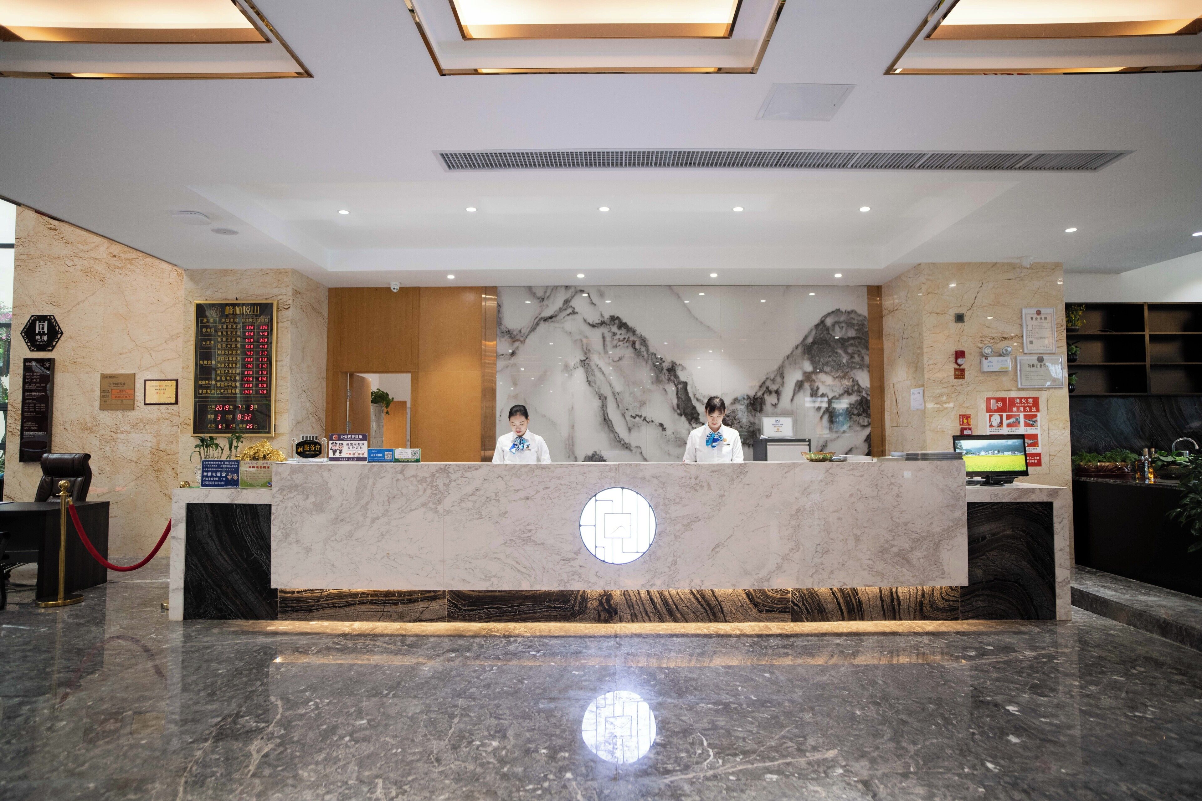 Zona de recepción de hotel con mostradores de mármol, una pantalla digital y un recepcionista.