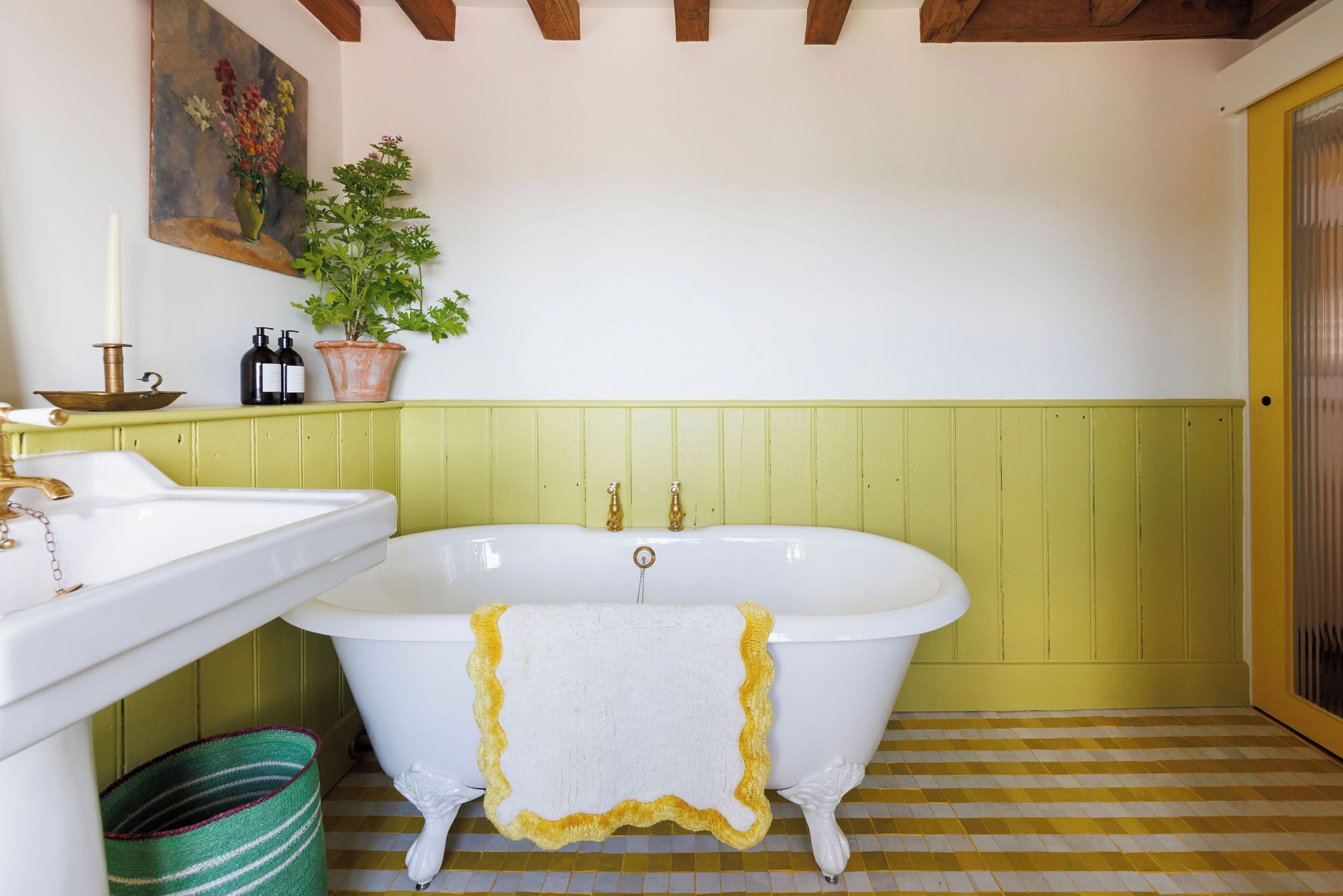 Een badkamer met een witte pootbad, een groen gestreept tapijt, een witte wastafel en een potplant.