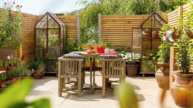 Une table en bois, entourée de chaises, se trouve dans un coin du jardin, délimité par une clôture en bois et agrémenté de plantes en pot.