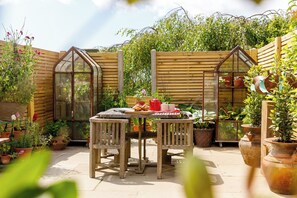 Een houten tafel met stoelen in een tuin, met houten omheining en bloempotten.