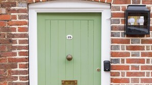 Une porte verte avec un heurtoir en laiton, une boîte aux lettres et une plaque d’immatriculation.