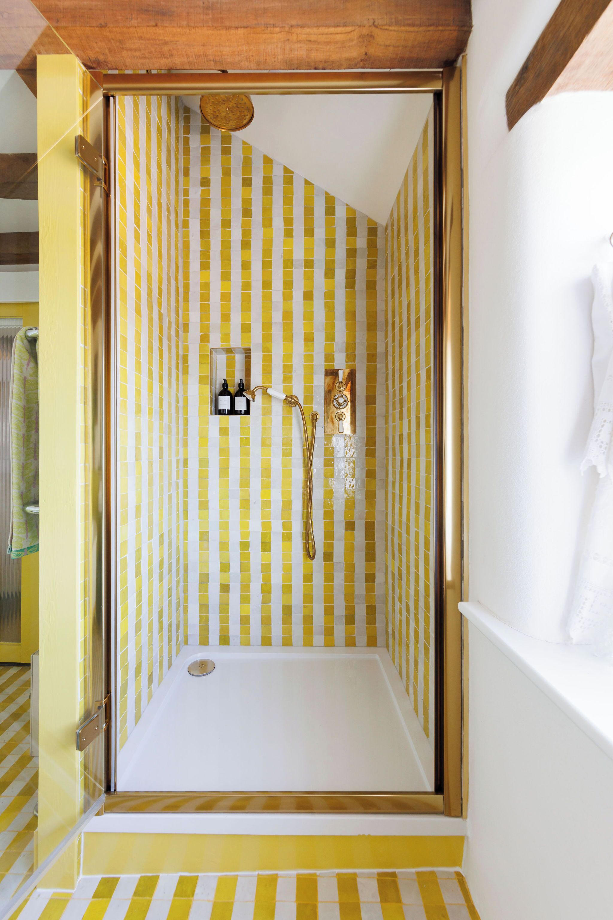 A shower with yellow and white striped tiles, a white bathtub, and a wooden ceiling.