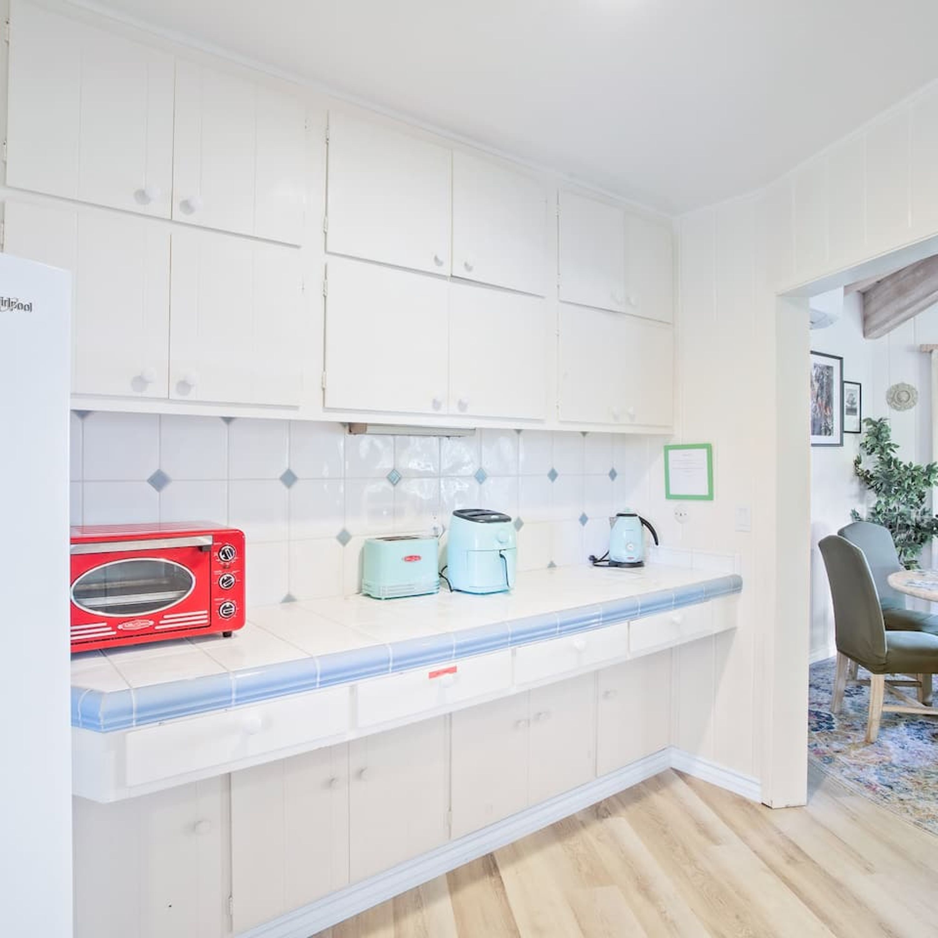 Una cucina con mobili bianchi, un tostapane rosso, un bollitore blu e un bollitore verde sul piano di lavoro.