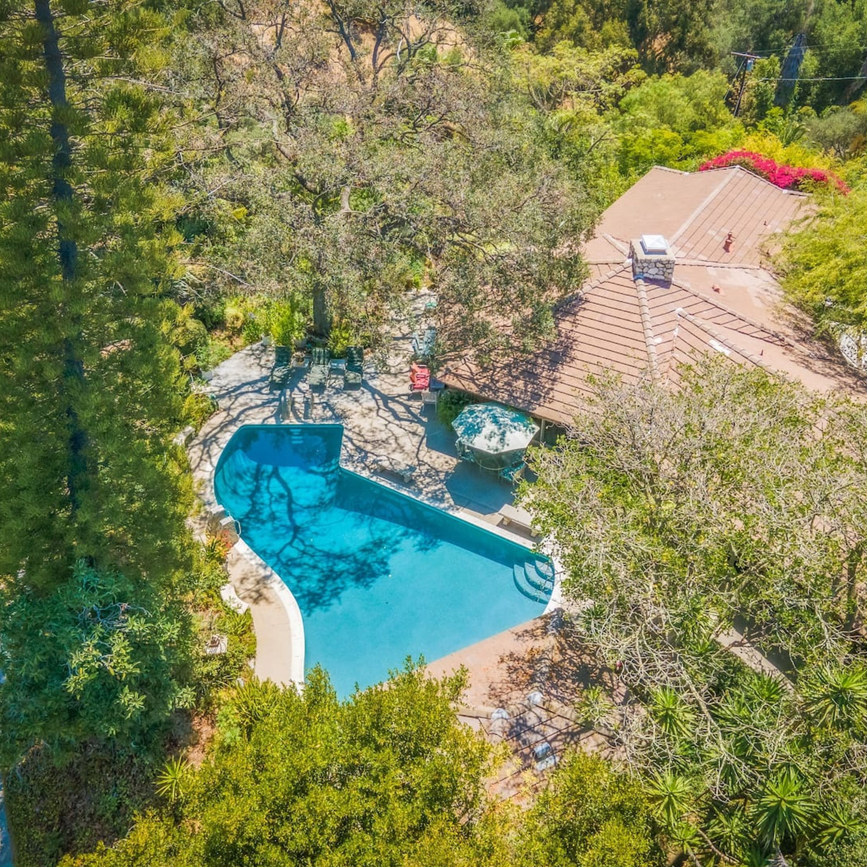 An aerial view of a property with a swimming pool surrounded by lush greenery, a covered patio area, and a stone structure.