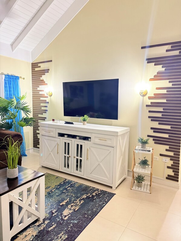 A living room with a TV mounted on a white cabinet, a brown sofa, a coffee table with a plant, and a patterned rug.