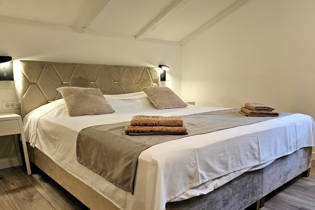 A neatly made bed with two pillows, a bedside table, and a lamp.