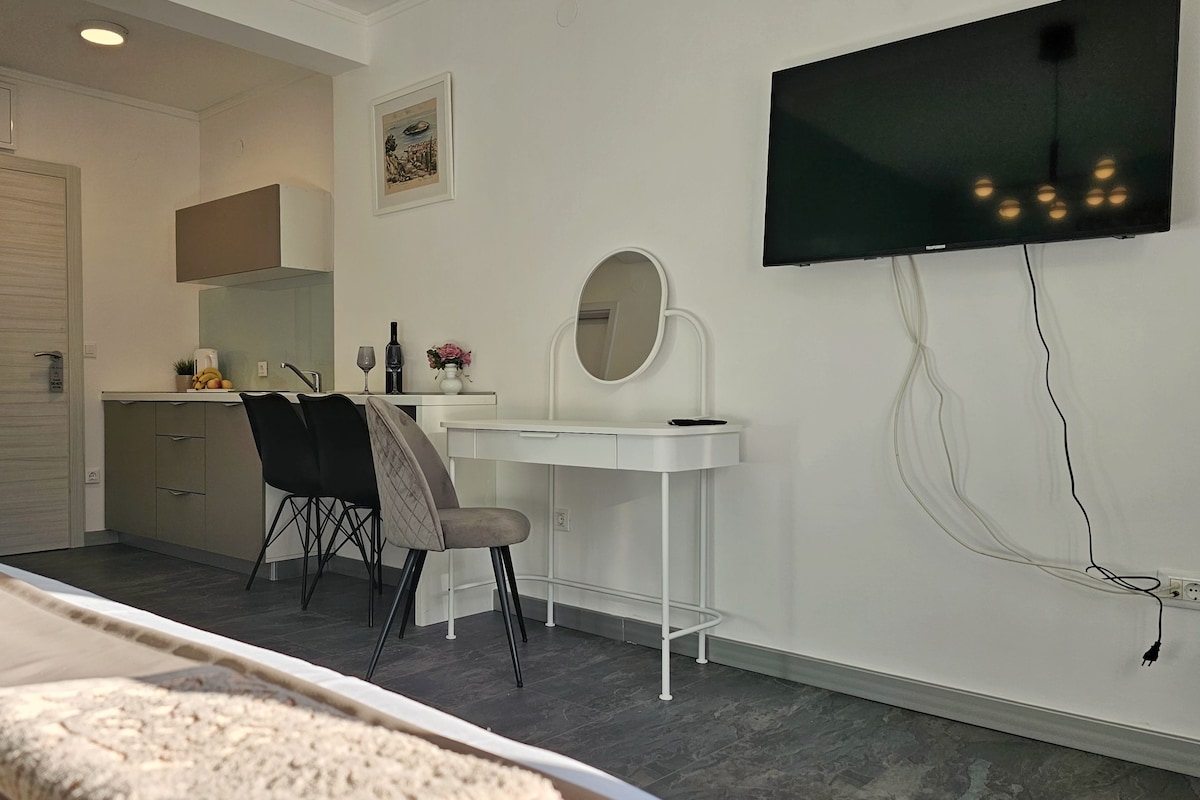 A modern bedroom with a bed, a desk, a chair, a TV, and a mirror.
