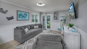 Un salon avec un canapé gris, un tapis à motifs et des œuvres d’art accrochées aux murs.