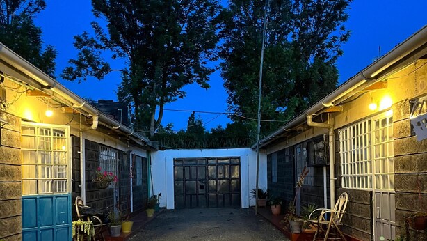 A courtyard with a gravel path, two buildings with barred windows, and potted plants.