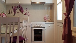 Una cocina compacta con armarios blancos, un horno empotrado y un muro decorativo con motivos florales.