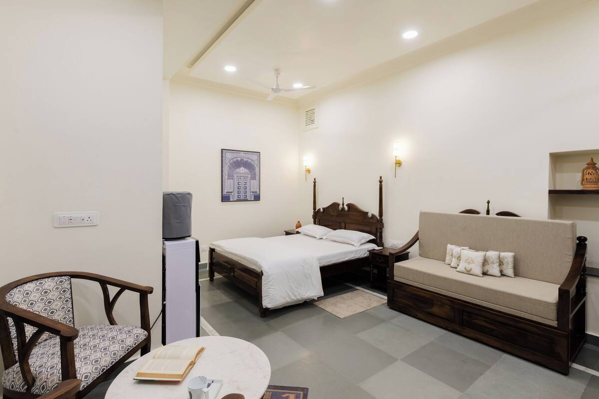 Un dormitorio con cama, sofá, sillón, una mesita y televisor.