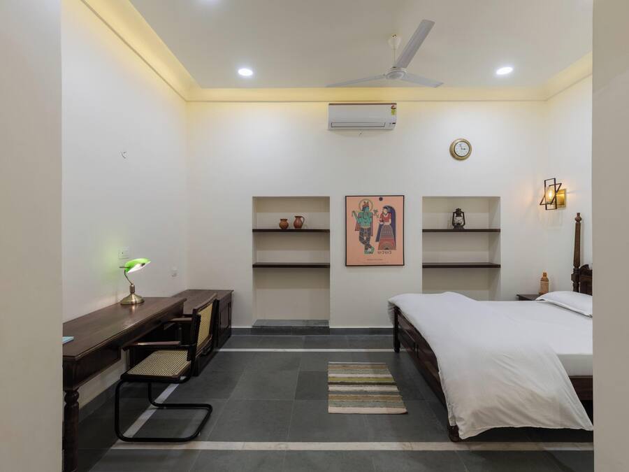 Une chambre à coucher comprenant un lit, un bureau, une chaise, des étagères et un ventilateur de plafond.