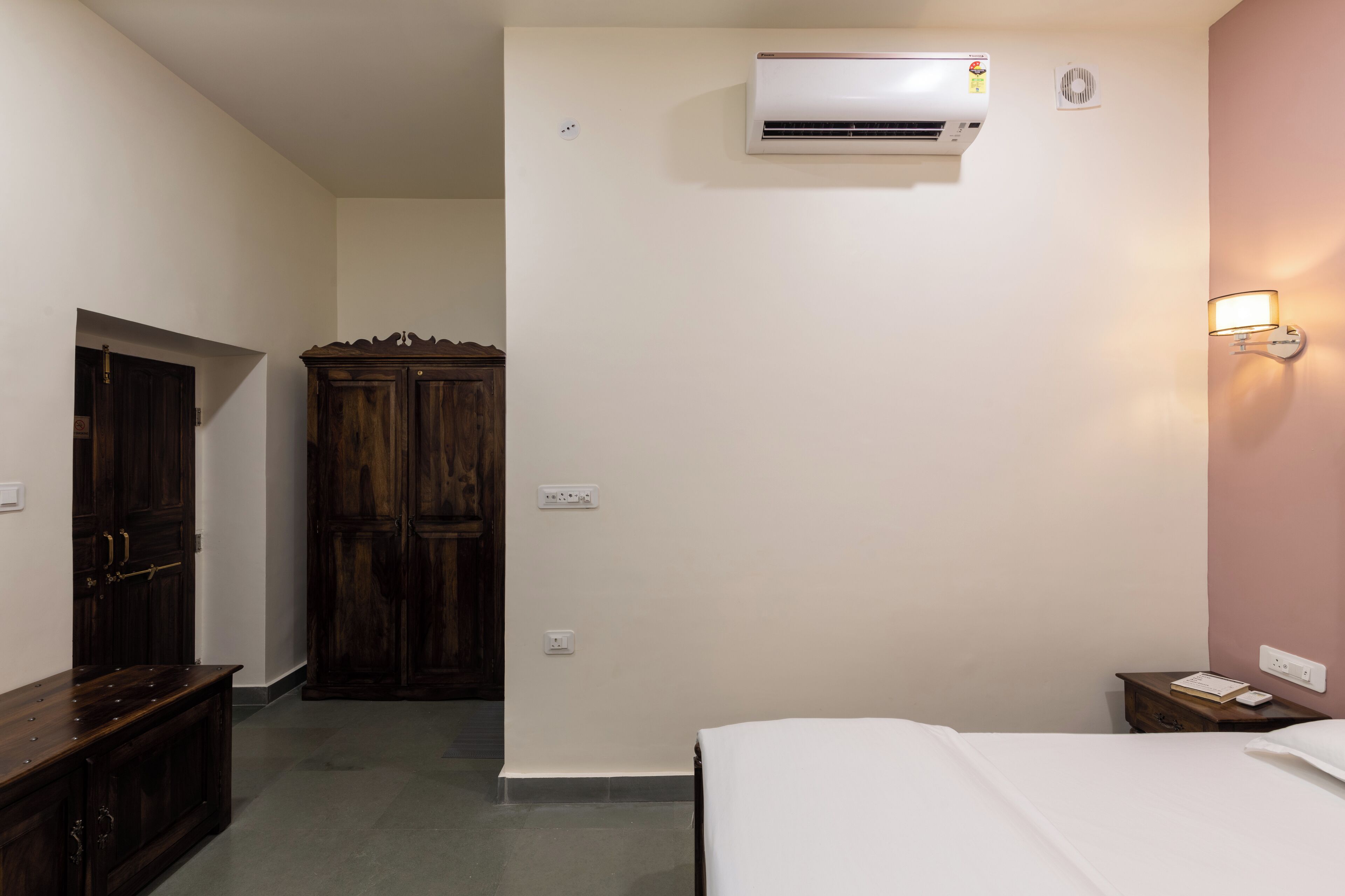 A bedroom with a bed, an air conditioning unit, a wardrobe, and a nightstand.