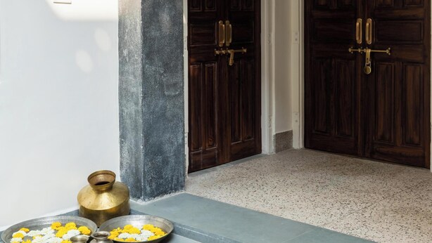 A traditional entrance with two dark wooden doors, a small wooden shelf, and a tiled floor with a decorative border. - Heart Of The City By Rashmi (Jaipur)
