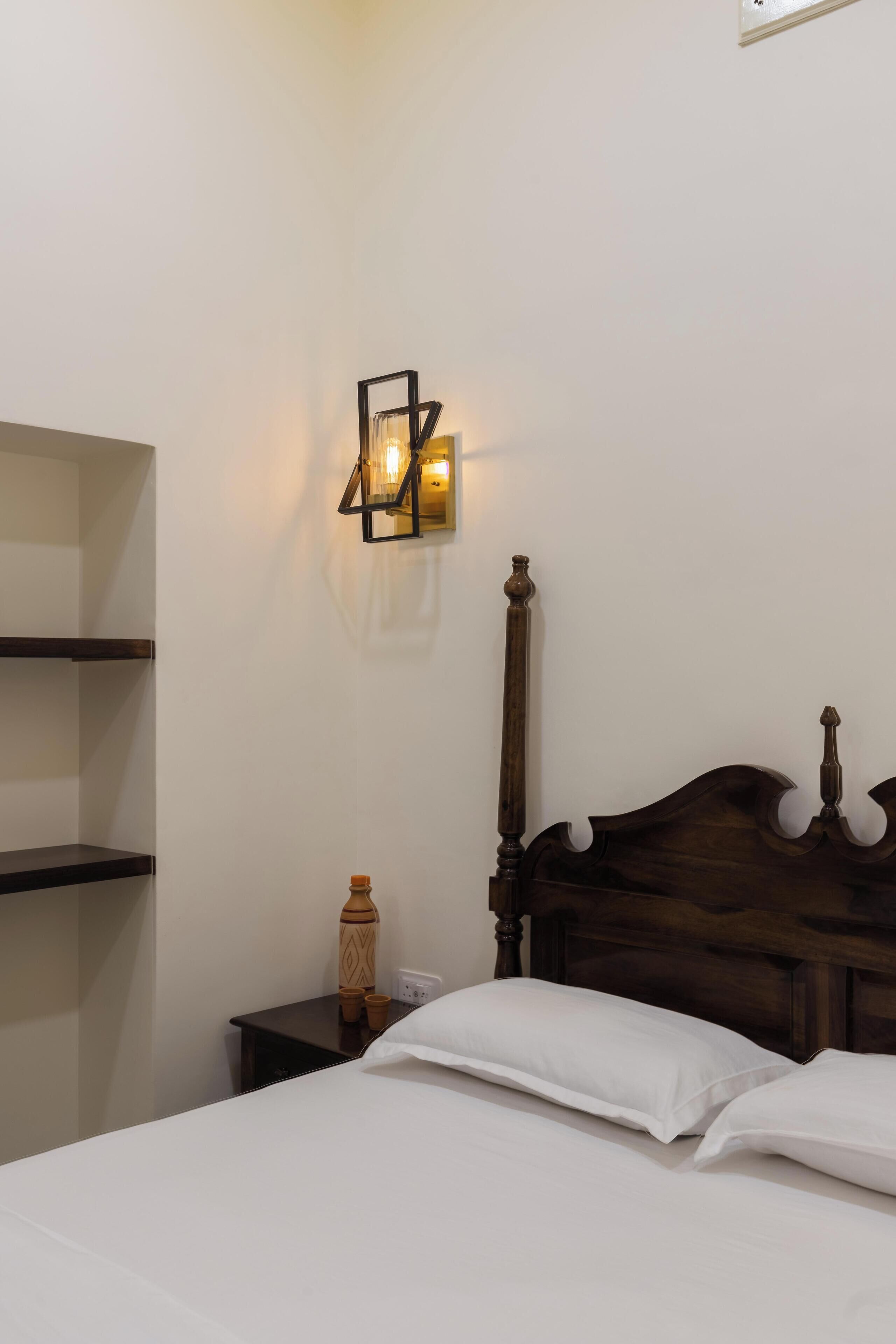 Cama bem arrumada com lençóis brancos, cabeceira de madeira e mesa de cabeceira com garrafa e copos.