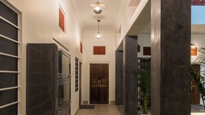 A hallway with a modern design, featuring a dark refrigerator, a wooden door at the end, and a potted plant on the right. - Heart Of The City By Rashmi (Jaipur)