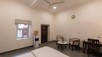 A hotel room with a bed, a ceiling fan, a small table with chairs, a refrigerator, and a window with a view.