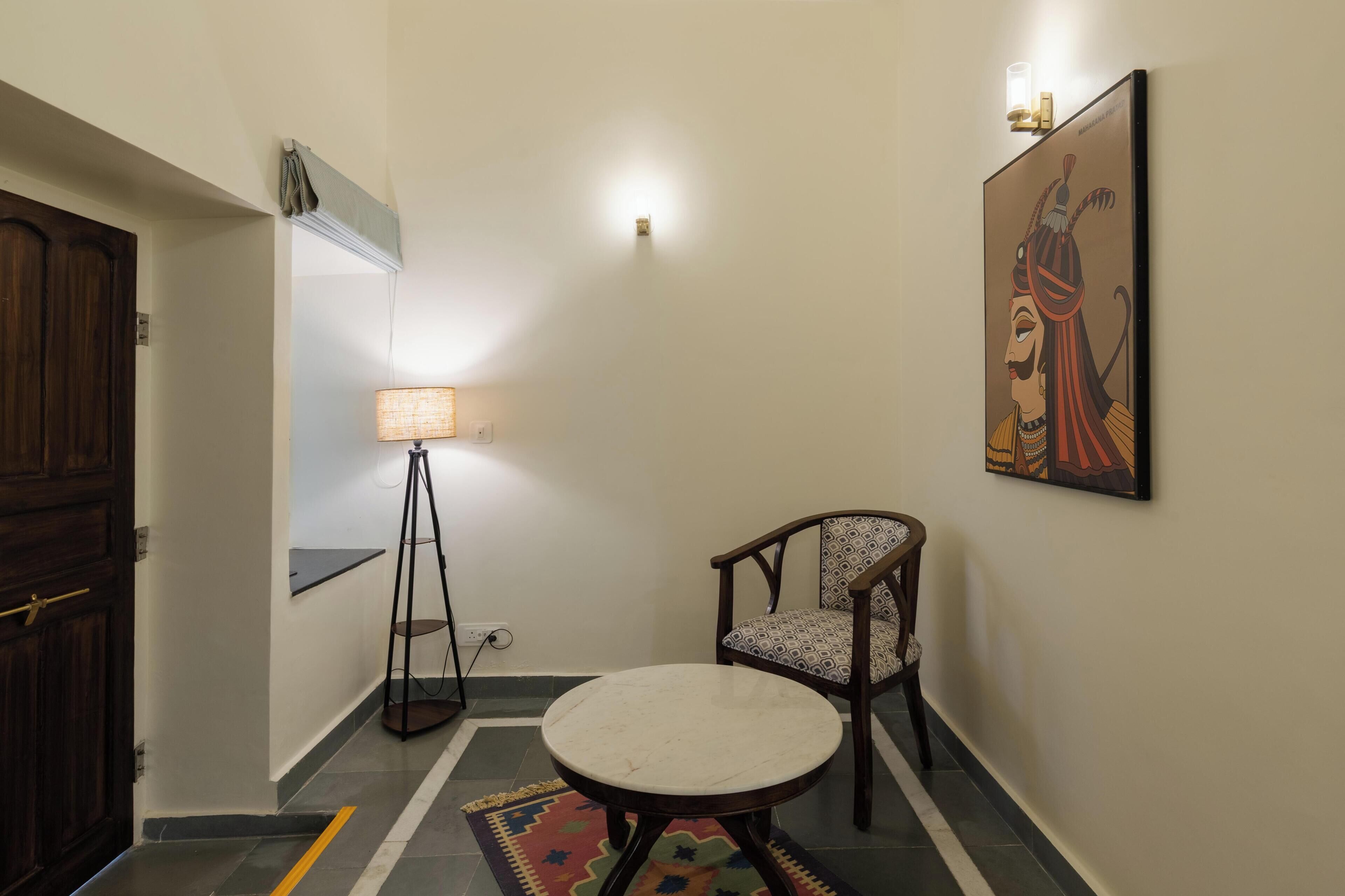 A hallway with a round table, a chair, a lamp, and a painting on the wall.