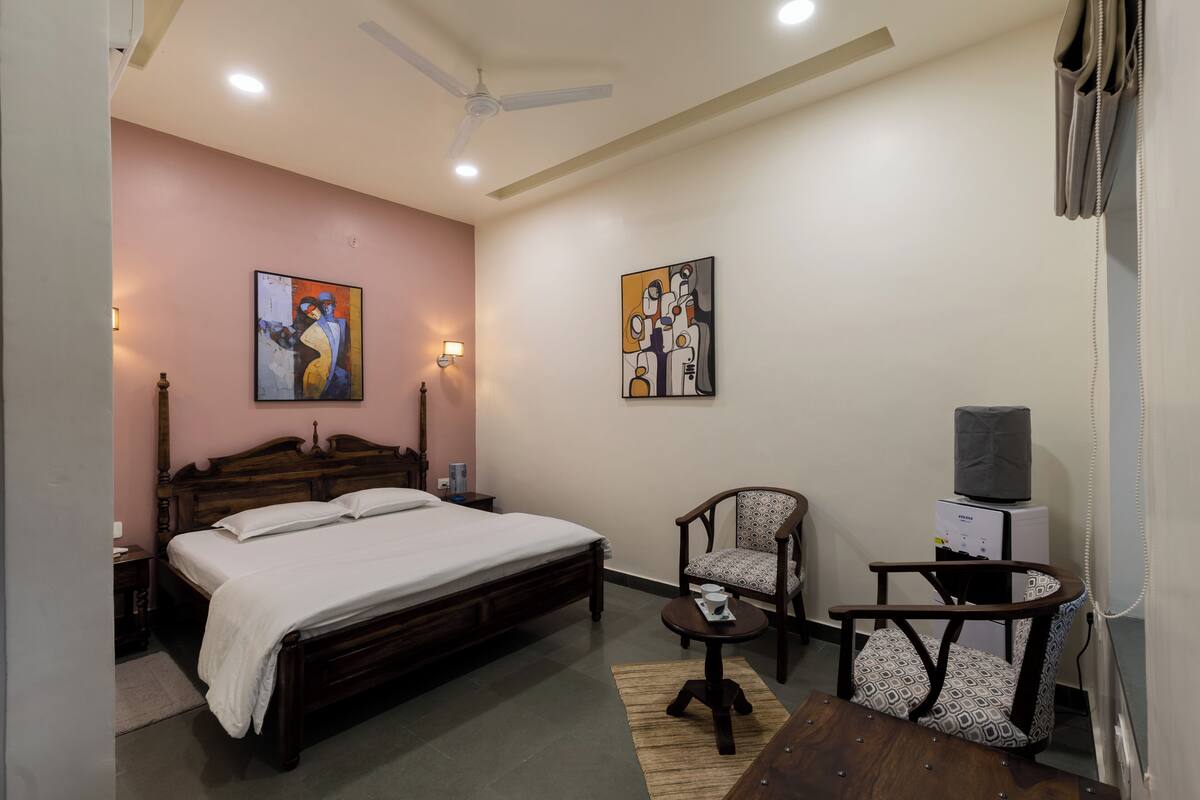 Un dormitorio con cama, una silla, una mesita, televisor y obras de arte en las paredes.