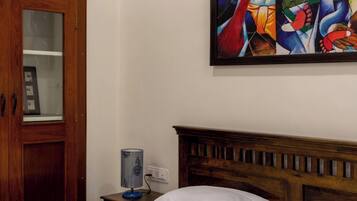 A bedroom with a wooden headboard, a bed with white linens, a nightstand with a lamp, and a wooden wardrobe with a glass door.