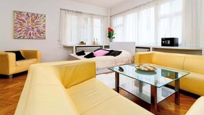 A modern living room with yellow sofas, a glass coffee table, and a bed with white bedding.