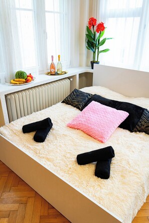 A bedroom with a bed, pillows, a fluffy rug, and a window with curtains.