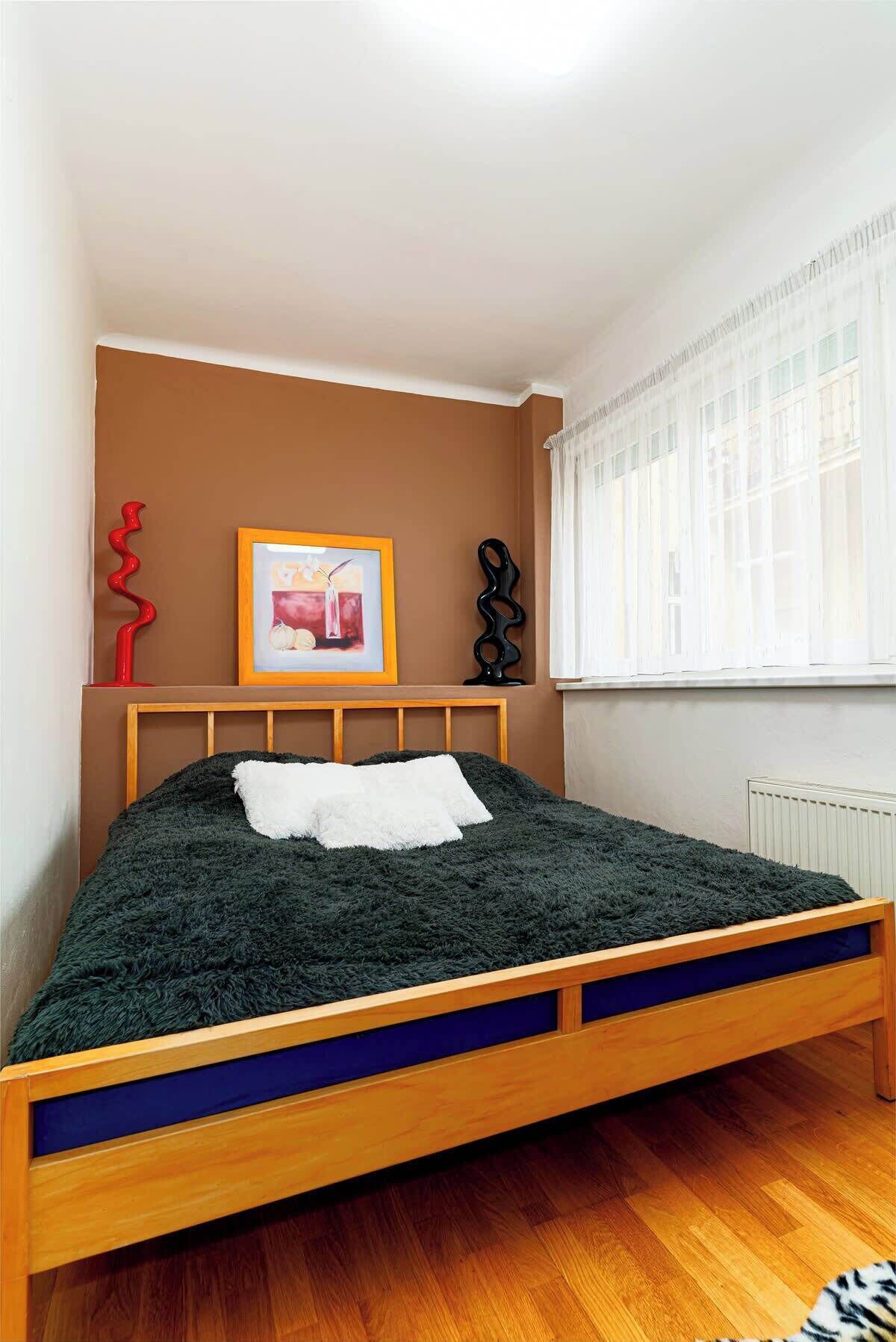 Quarto com cama de madeira, quadro na parede e janela com cortinas.